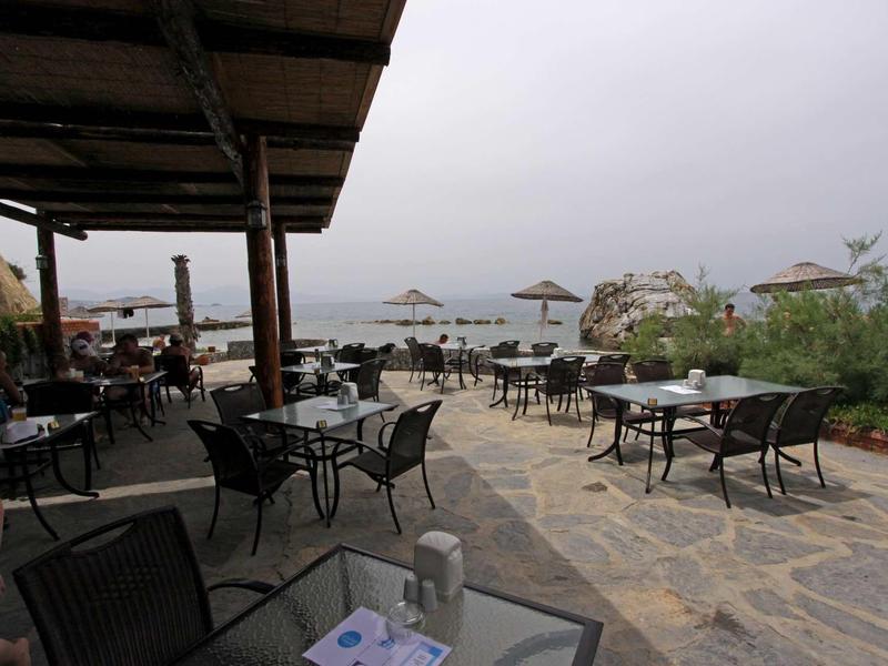 Terrace with tables and chairs by the sea under a cloudy sky.