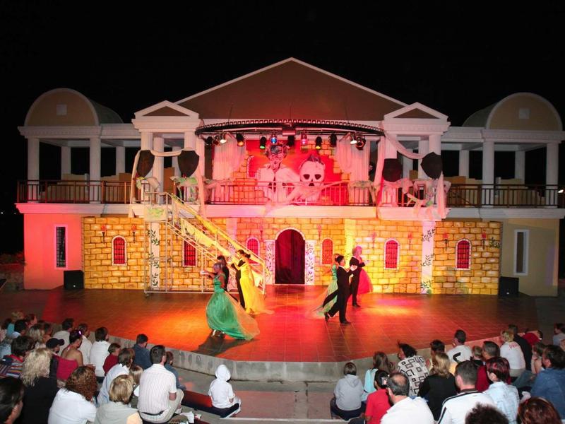 Theater performance in front of a large illuminated building facade set with outdoor audience.