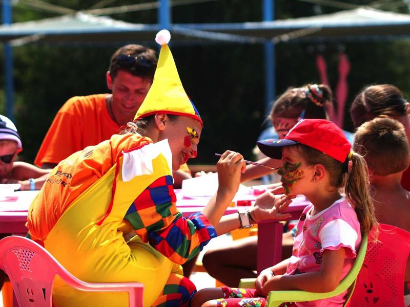 Children and a clown in colorful costume sit at a table, likely during a hotel activity.