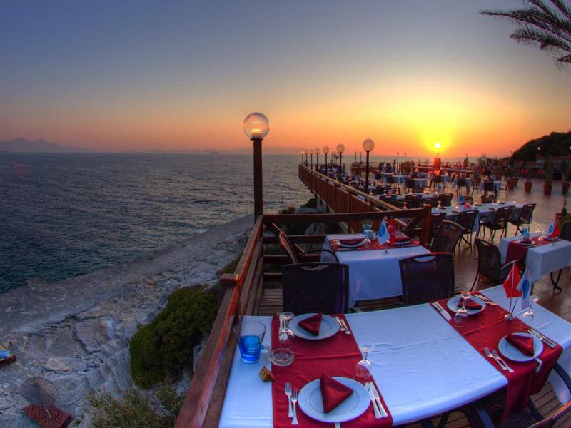 Outdoor seating by the sea at sunset with tables set in red and white linens.