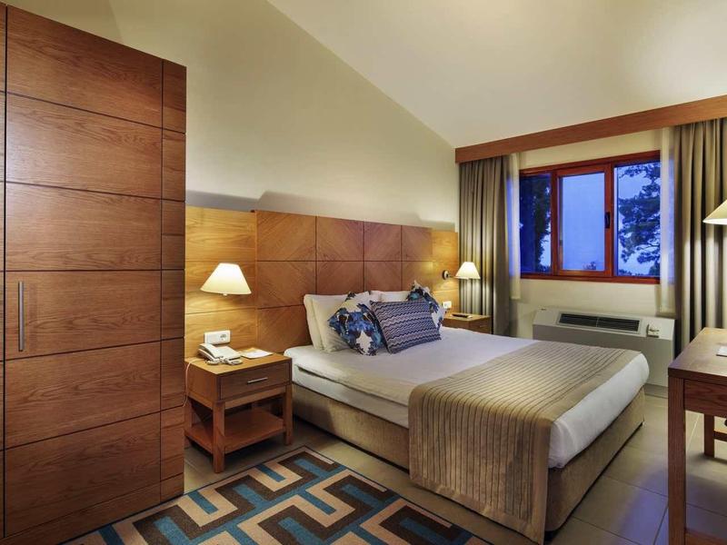 Cozy hotel room with double bed, wooden furniture, and window with a view of trees.