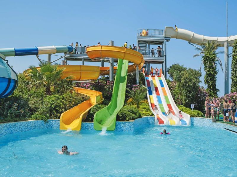 Several colorful water slides lead into a large pool with people swimming.
