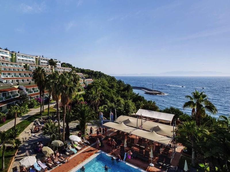 Hotel complex with pool, palm trees, and ocean view under clear sky.