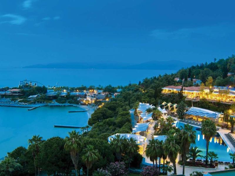 Hilltop hotel resort with pool and sea view under blue sky at sunset.