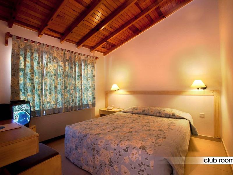 Cozy hotel room with wooden beam ceiling, floral curtains, and double bed.