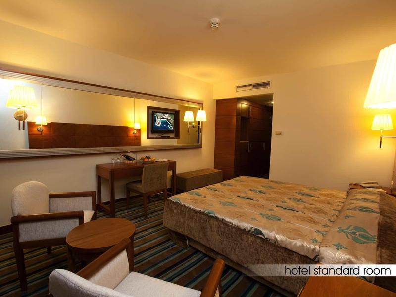 Standard room with double bed, desk, chairs, TV, and warm lighting.