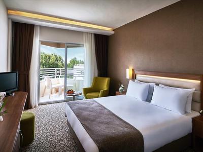 Modernes Hotelzimmer mit Doppelbett, Balkon und Sitzbereich mit grünem Sessel.