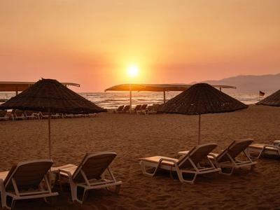 Lehátka pod slunečníky na pláži při západu slunce s výhledem na moře.