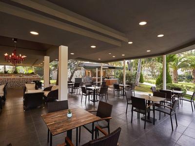 Terasa hotelové restaurace s dřevěnými stoly a výhledem na zelenou zahradu.