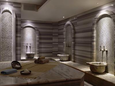 Interiér hammamu s kamennými zdmi, koryty a tlumeným osvětlením.