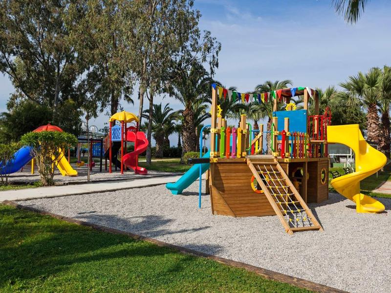 Barevné venkovní hřiště s tobogány a dřevěnými strukturami v zeleném parku.