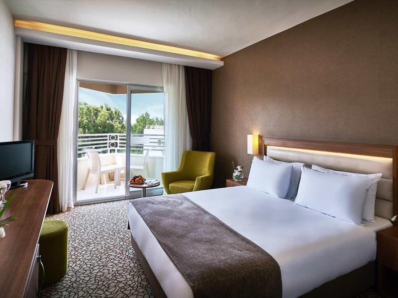 Moderní hotelový pokoj s manželskou postelí, balkonem a zeleným výhledem.