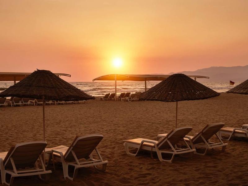 Lehátka pod slunečníky na pláži při západu slunce s výhledem na moře.