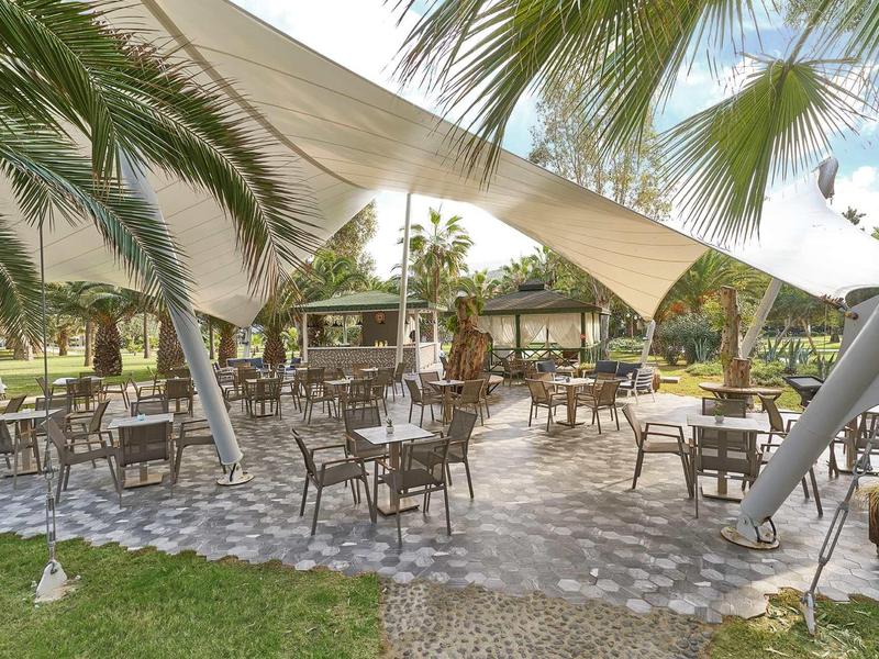 Venkovní terasa s stoly a židlemi pod bílým baldachýnem.