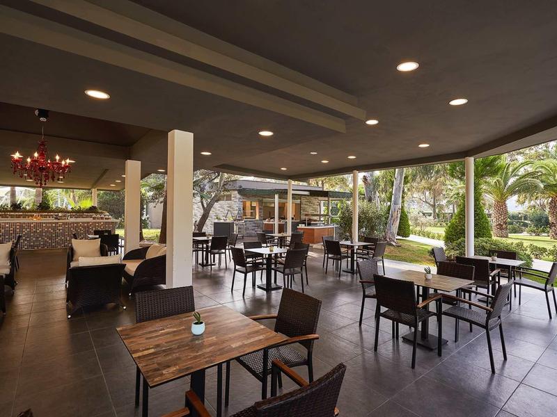 Terasa hotelové restaurace s dřevěnými stoly a výhledem na zelenou zahradu.