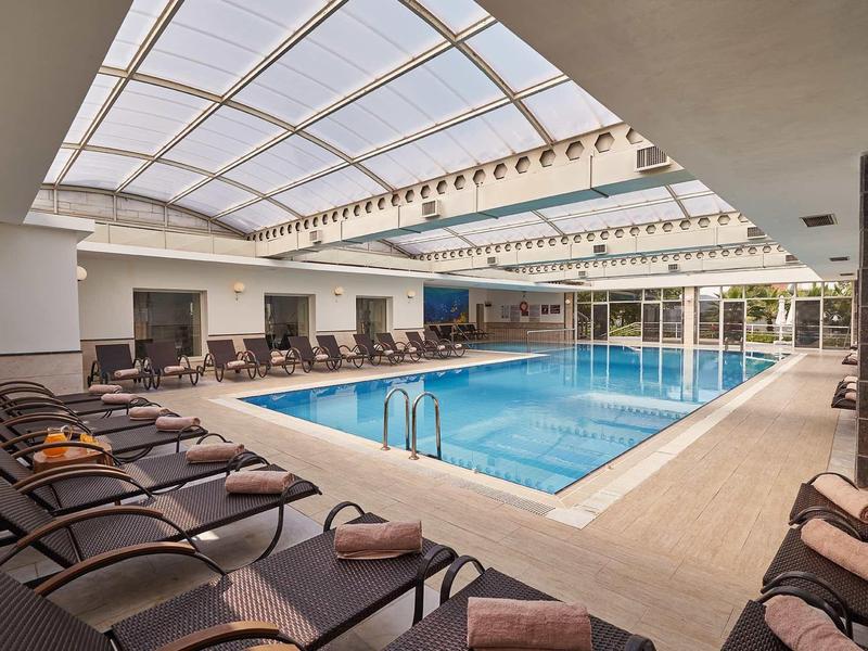 Světle krytý bazén s lehátky a průhlednou skleněnou střechou.