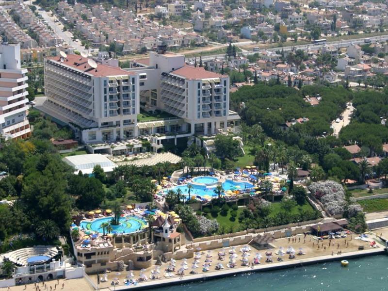 Großes Hotel mit mehreren Poolanlagen, Palmen und Strand an Küste in urbaner Umgebung.