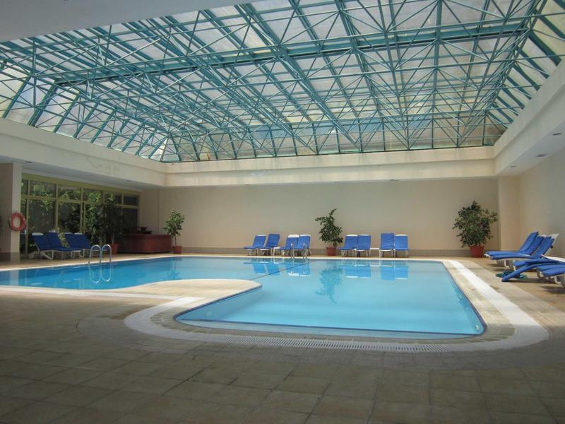 Innenhallen-Schwimmbad mit klarem Wasser, blauen Liegestühlen und Glasdach für Tageslicht.