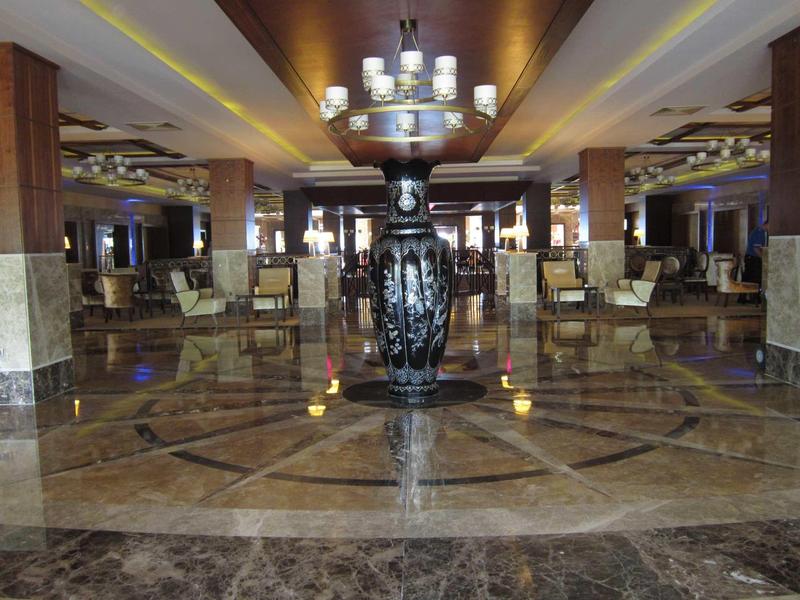 Große Hotellobby mit glänzendem Marmorboden und einer kunstvollen Vase als Mittelpunkt.