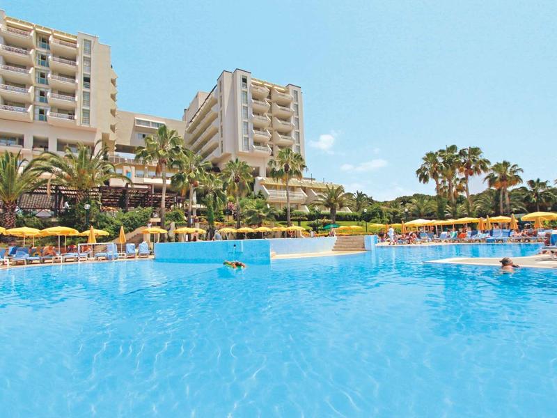 Großer blauer Hotelpool mit Liegestühlen, Sonnenschirmen und Palmen vor hohen Gebäuden.