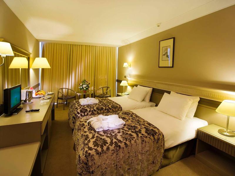 Gemütliches Hotelzimmer mit zwei Betten, warmem Licht, Vorhängen und Teppichboden.