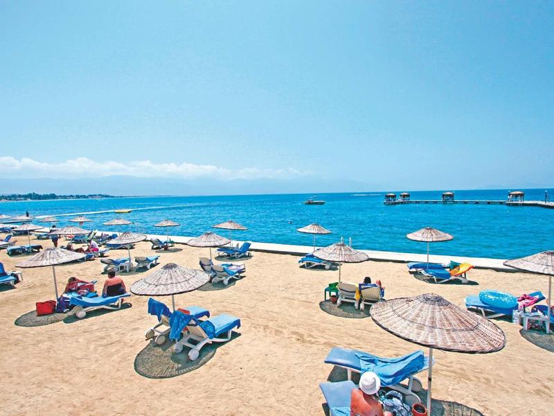 Strand mit Liegestühlen und Sonnenschirmen, blauer Himmel und ruhiges Meer im Hintergrund.