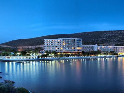 Modern hotel building lit up along a calm shoreline at dusk.