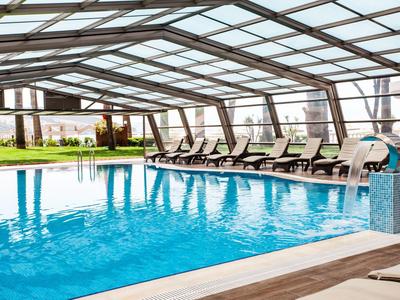 Heated indoor pool with lounge chairs under a transparent roof at a hotel.
