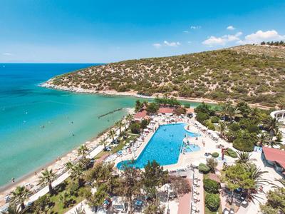 Hotel complex with large pool and sea view at a sunny beach.
