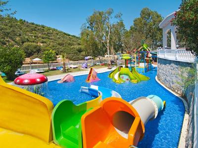 Colorful water playground with slides in a pool surrounded by nature and umbrellas.