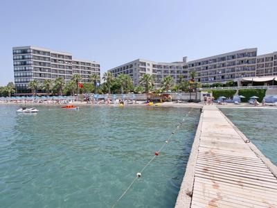 View of a modern hotel by the water with a pier and sun loungers on the beach.