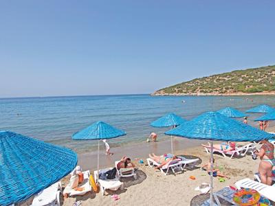 Beach with blue umbrellas and sun loungers beside calm sea and green hill.