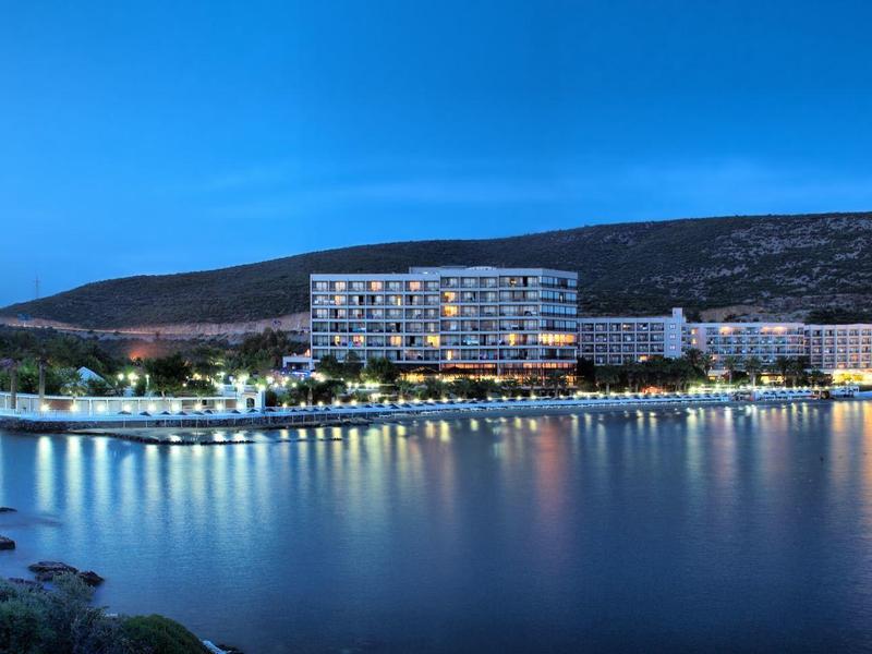 Modern hotel building lit up along a calm shoreline at dusk.