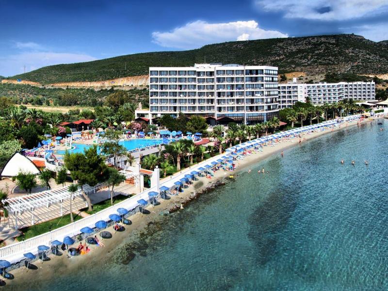 Large beachfront hotel with pool, sun umbrellas, and clear seawater on a sunny day.
