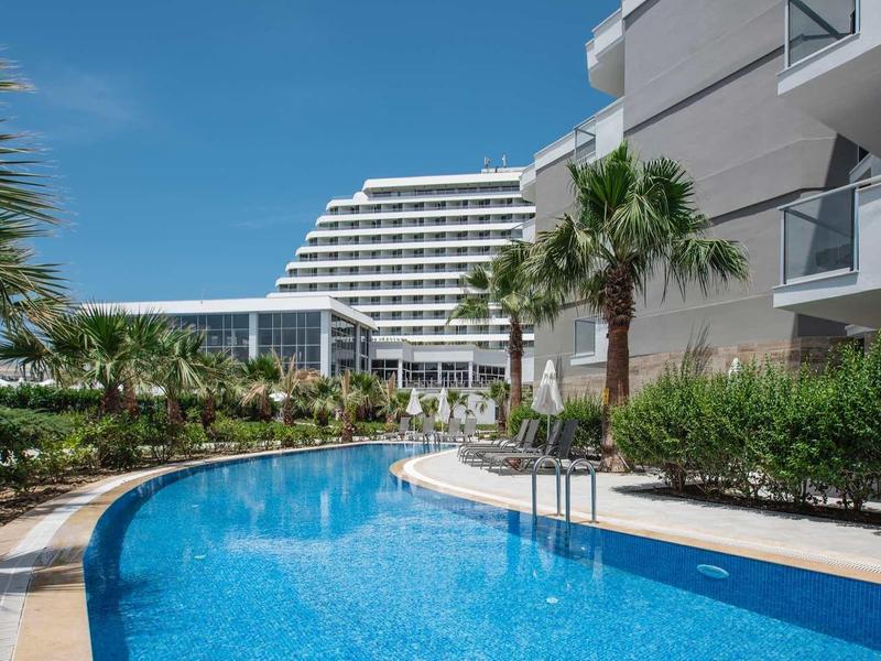 Modern outdoor pool with palm trees and hotel building under clear sky.
