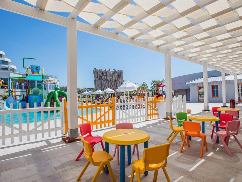 Colorful chairs and tables on a covered terrace overlooking a water park and hotel building.