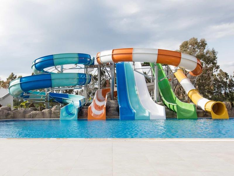Several colorful water slides lead into a large pool under a cloudy sky.