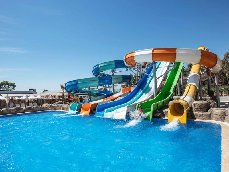 Several colorful water slides lead into a large blue swimming pool on a sunny day.