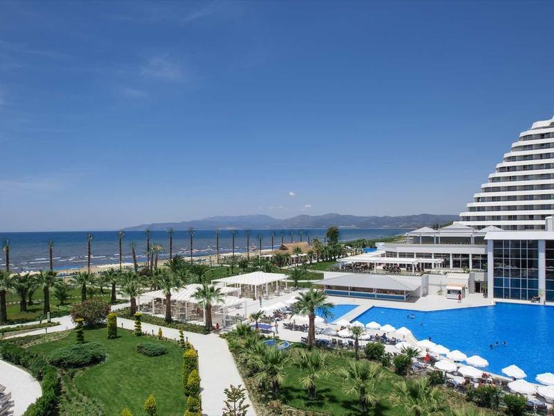 Modern hotel with large pool, sun umbrellas, and view of blue sea under clear sky.