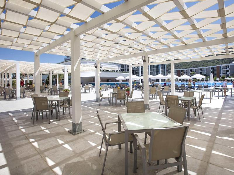 Covered terrace with tables and chairs next to a pool at a holiday resort.