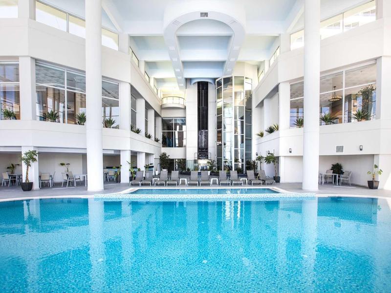 Brightly lit indoor pool in modern hotel with white walls and glass windows.