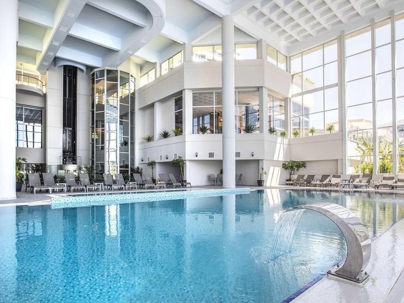 Modern indoor pool with large windows and cozy seating areas in a hotel.