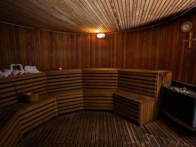 Sauna acogedora de madera con bancos para sentarse, iluminación y utensilios típicos de sauna.