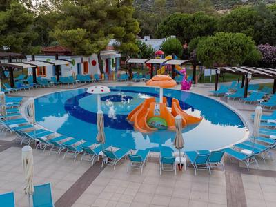 Piscina exterior redonda con tobogán acuático y tumbonas en un complejo hotelero con árboles.