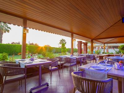 Restaurante al aire libre con mesas preparadas y vista a setos verdes al atardecer.