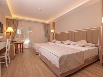 Helles Hotelzimmer mit zwei großen Betten, Holzfußboden und Fenster mit Vorhängen.