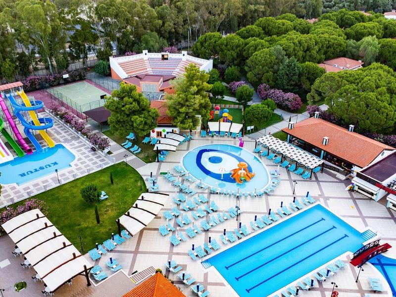 Vista aérea de un hotel con piscinas, toboganes de agua y tumbonas, rodeado de árboles.