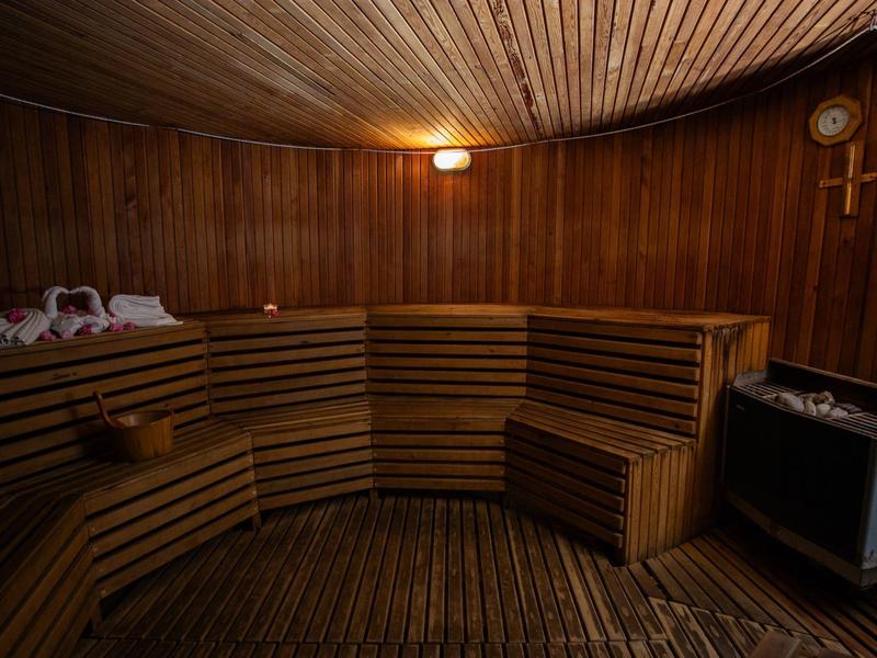 Sauna acogedora de madera con bancos para sentarse, iluminación y utensilios típicos de sauna.