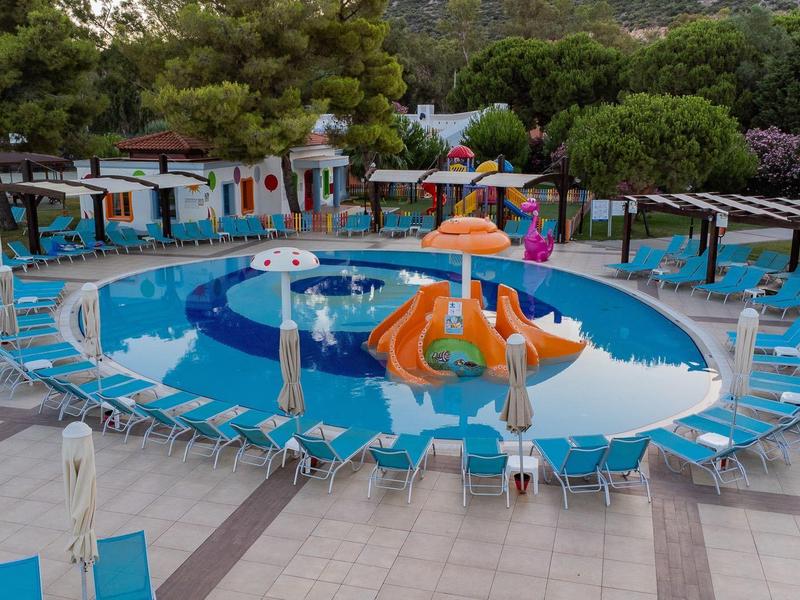 Piscina exterior redonda con tobogán acuático y tumbonas en un complejo hotelero con árboles.