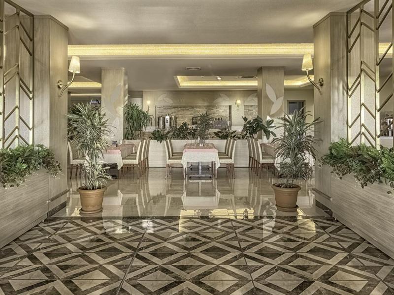 Área elegante del vestíbulo del hotel con suelo de mármol, plantas y asientos en colores neutros.